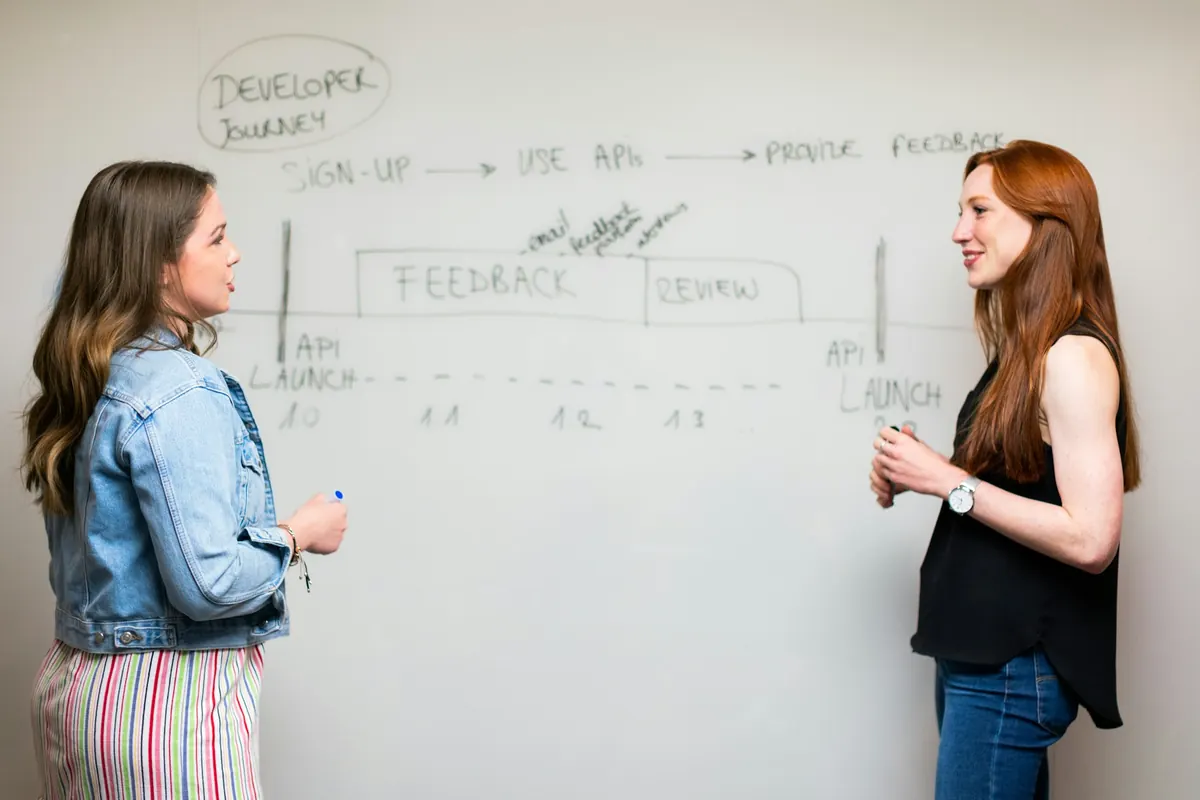 Deux femmes discutent devant un tableau blanc où est dessiné le déroulé d'un projet