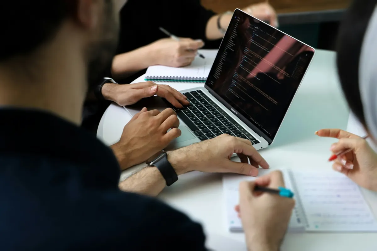 Trois personnes autour d'un ordinateur portable affichant du code, carnets ouverts