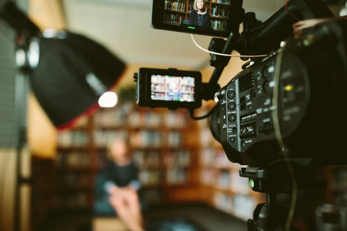 Une caméra de tournage cadre une personne assise devant une bibliothèque