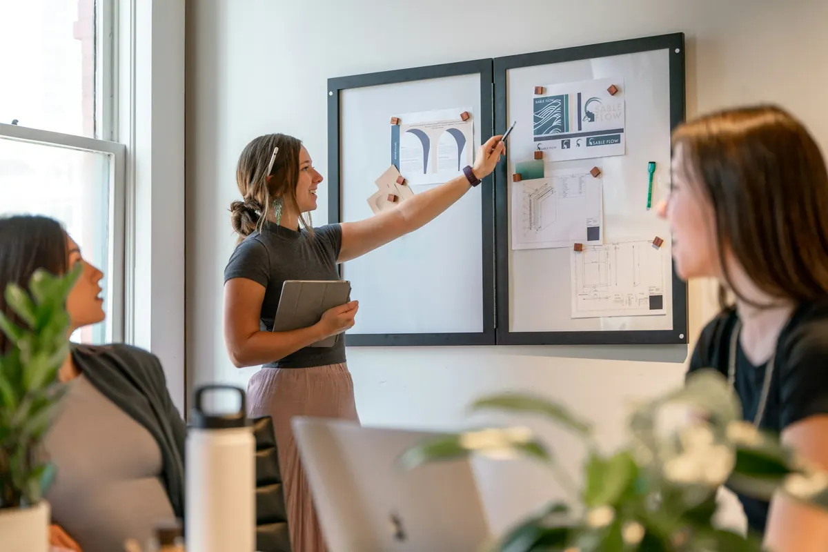 Une femme présente des maquettes affichées au mur à ses collègues